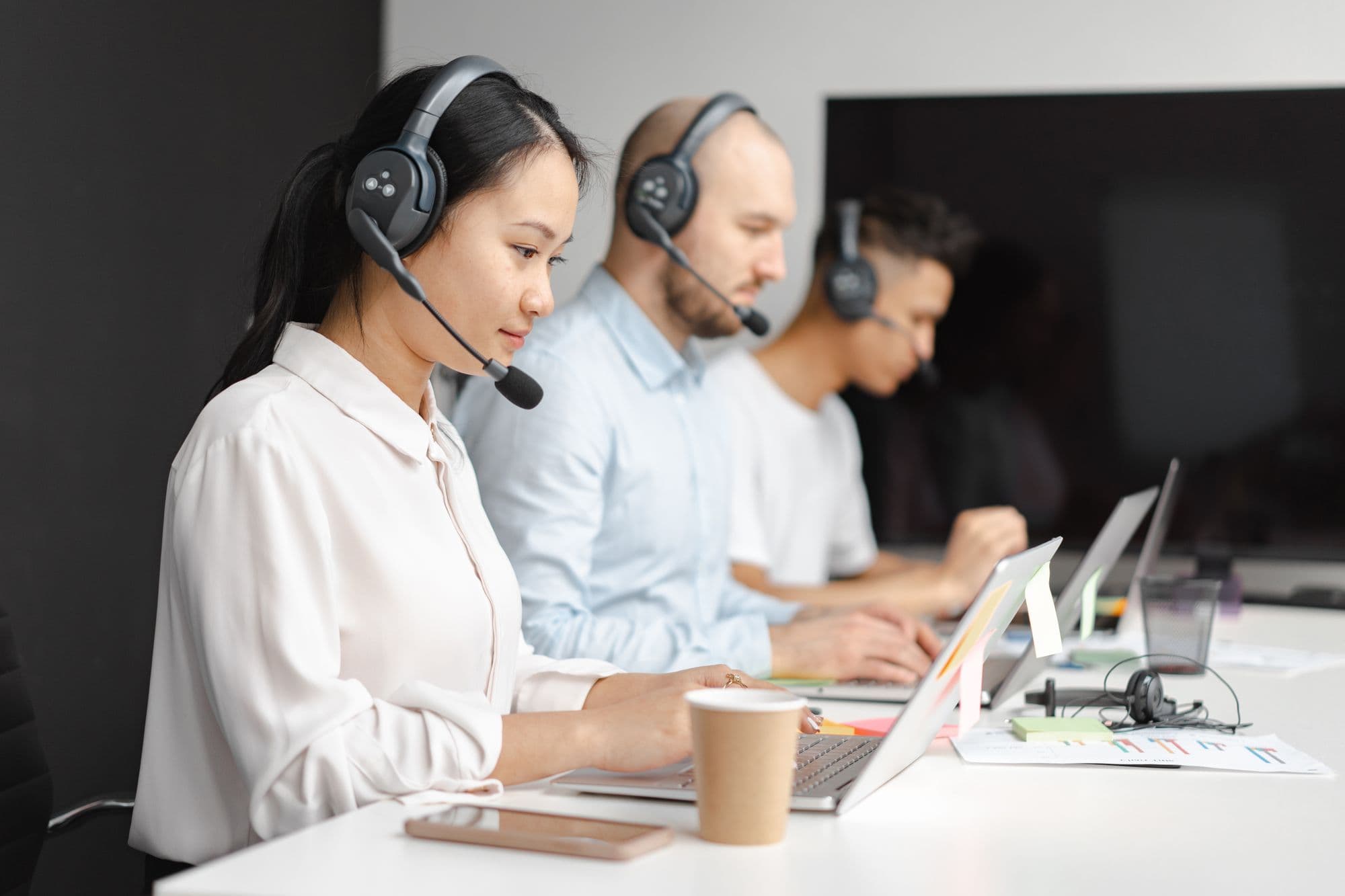 Three virtual assistants wearing headsets, working side by side at laptops